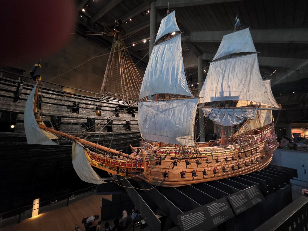 Modell der Vasa mit gesetzten Segeln vor dem originalen Kriegsschiff im Vasa-Museum.