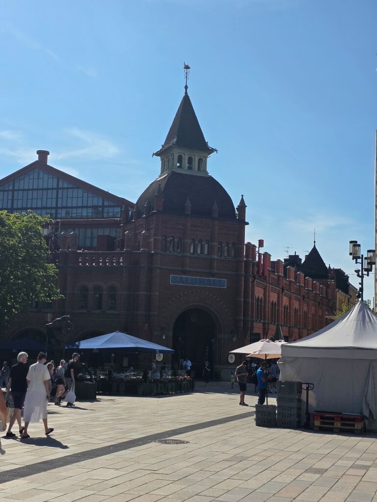 Historische Markthalle Östermalms Saluhall in Stockholm mit Backsteinfassade und belebtem Vorplatz.