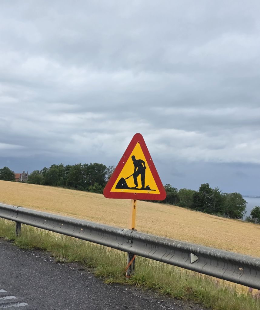 Schwedisches Baustellenschild am Straßenrand vor dunklem Regenhimmel