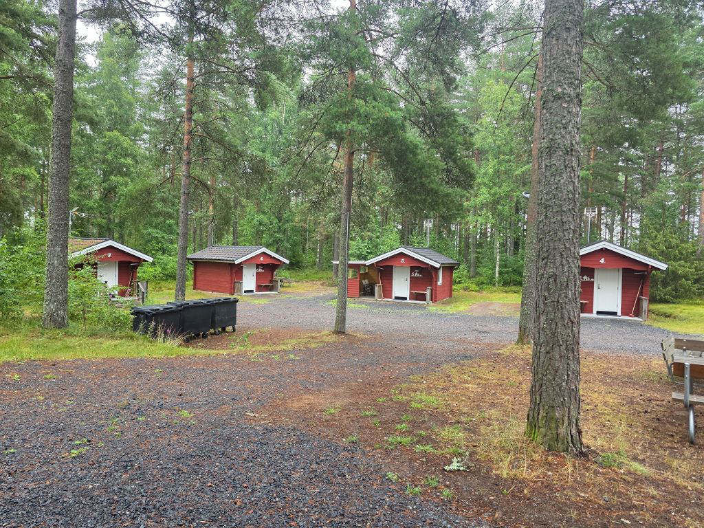 Mehrere kleine rote Holzhütten zwischen hohen Bäumen im Hyltena Stugby bei Jönköping