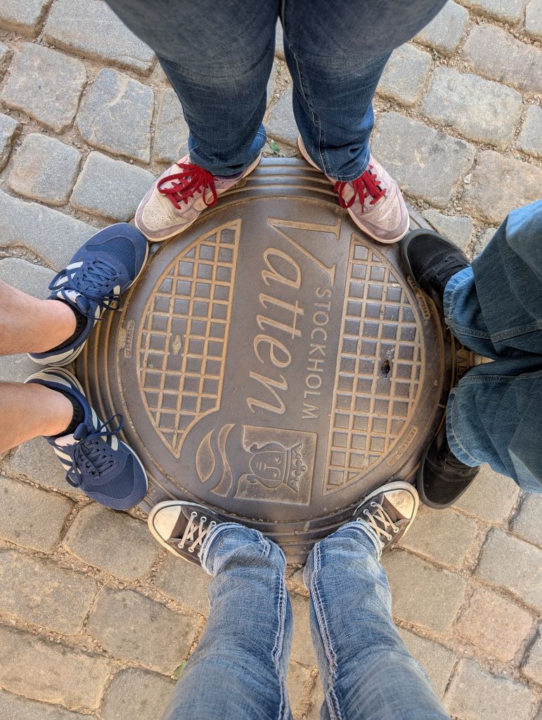 Unsere Schuhe rund um einen Gullideckel mit Stockholm-Schriftzug auf dem Kopfsteinpflaster.