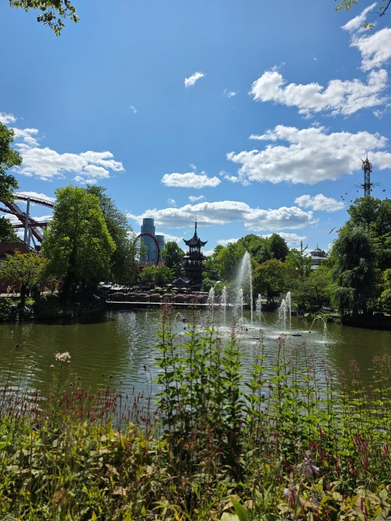 See mit Springbrunnen und üppiger Bepflanzung im Tivoli Kopenhagen bei strahlendem Sonnenschein.