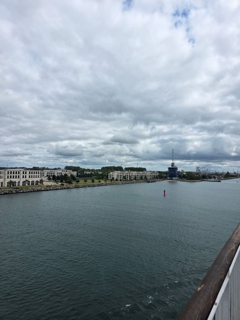 Blick von der Fähre auf den Hafen von Rostock unter grauem Wolkenhimmel.
