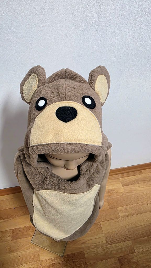 Nahaufnahme der Bärenkapuze eines handgenähten Kinderkostüms aus Fleece mit beigefarbenen Ohren, großer Schnauze, schwarzer Nase und Augen mit weißen Druckknöpfen.